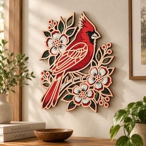 May include: A layered wooden wall art piece featuring a bright red cardinal bird perched on a branch surrounded by white flowers with red centres and green leaves. The design uses multiple stacked wood layers to create a dimensional effect.