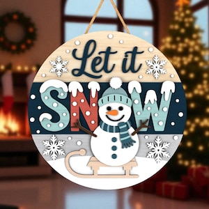 May include: A circular wooden sign with the words "Let it Snow" in a winter theme. The sign features a snowman wearing a hat and scarf, snowflakes, and a sled. The sign is suspended by a rope.