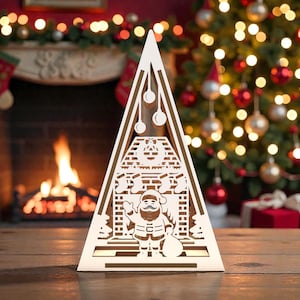 May include: A white, laser-cut Christmas decoration in the shape of a tree. The design features Santa Claus, stockings, and a fireplace. The background includes a decorated Christmas tree and a fireplace with a fire.