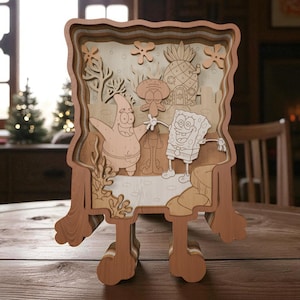 Könnte beinhalten: Ein mehrschichtiges Holzkunstwerk mit Charakteren aus der Zeichentrickserie SpongeBob Schwammkopf. Das lasergeschnittene Design zeigt SpongeBob, Patrick und Thaddäus. Das Stück ist braun und beige und wird von einem Ständer getragen.