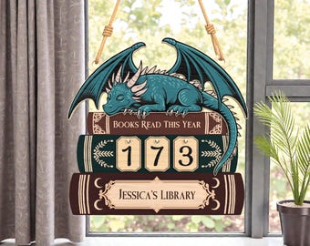 May include: Wooden sign with a teal dragon on three stacked books. The books read "BOOKS READ THIS YEAR", "173", and "JESSICA'S LIBRARY". The sign is suspended by natural rope.