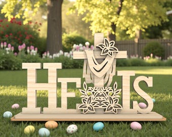 May include: Wooden Easter decoration with the words "HE IS" in large block letters. A wooden cross with floral accents and decorative Easter eggs are also included. The scene is set on a grassy lawn with a blurred background of trees and flowers.