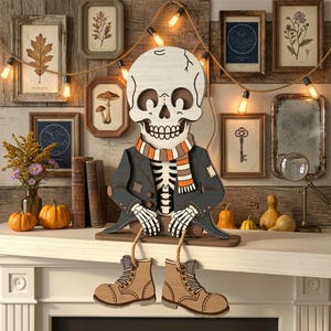 May include: A wooden skeleton figurine featuring a white skull, a dark gray jacket with patches, and a striped orange, white, and brown scarf. The skeleton has dangling legs attached by rope, wearing tan boots, and sits on a flat wooden base.