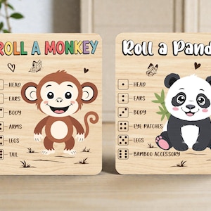 Pode incluir: Duas tábuas de jogo de madeira com o texto "Roll a Monkey" e "Roll a Panda". A tábua do macaco apresenta um macaco de desenho animado, e a tábua do panda apresenta um panda. Ambas as tábuas têm dados e etiquetas de partes do corpo.