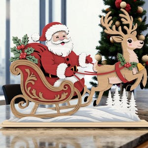 Op de afbeelding: Houten kerstdecoratie met de kerstman in een rode slee getrokken door een rendier. Het rendier is lichtbruin met een rode tuig en een gouden bel. De slee is rood met gouden accenten en de basis is lichtbruin.