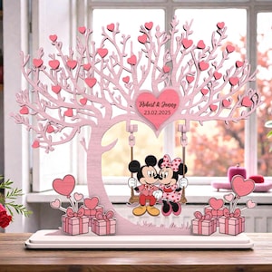 May include: A pink wooden tree decoration with heart-shaped leaves and a heart-shaped sign that reads "Robert & Jenny 23.02.2025". Mickey and Minnie Mouse are on a swing. Pink gift boxes and heart balloons are at the base.