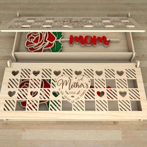 May include: Wooden box with a decorative lid, featuring a laser-cut design. The box contains a red rose and the word "mom". The front of the box has the text "A Mother's love is the heart of the family".