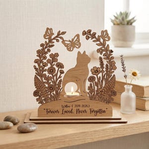 Peut inclure: Un bougeoir commémoratif en bois brun clair avec une silhouette de chat découpée au laser entourée de fleurs et de papillons. La base est gravée du texte Willow (2014-2026) et Forever Loved, Never Forgotten, avec une bougie chauffe-plat allumée.