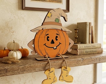 May include: A wooden pumpkin decoration featuring a smiling face, a tan witch hat with green and yellow patches, and dangling legs with yellow boots. The pumpkin is orange with black facial features and is designed to sit on a flat surface.