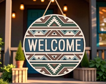 Puede incluir: Cartel de bienvenida redondo de madera con diseño geométrico en tonos marrón, verde y azul. La palabra «WELCOME» en letras blancas sobre fondo azul. El cartel cuelga de una cuerda natural, ideal para la puerta.