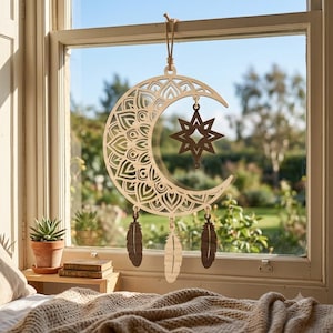May include: A laser-cut wooden wall hanging featuring a crescent moon with intricate mandala patterns. A dark brown eight-pointed star hangs from the centre of the moon, and three wooden feathers are suspended from the bottom edge by small rings.