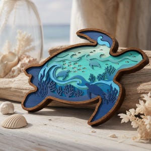 May include: A wooden, layered sea turtle art piece. The artwork features a detailed ocean scene with turtles, fish, and coral in shades of blue and teal. The outer frame is a dark brown, and the piece is displayed on a wooden surface.