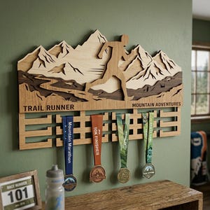 Może przedstawiać: Drewniany wyświetlacz medali biegacza górskiego z motywem górskiej sylwetki. Na wyświetlaczu widnieją napisy "TRAIL RUNNER" i "MOUNTAIN ADVENTURES". Cztery medale wiszą na wyświetlaczu, z niebieskimi, pomarańczowymi i zielonymi wstążkami.