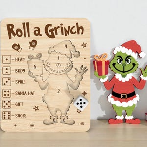 Könnte beinhalten: Weihnachtsspiel aus Holz mit dem Text "Roll a Grinch" und einer Grinch-Figur. Eine separate Grinch-Figur im Weihnachtsmann-Kostüm ist ebenfalls vorhanden. Das Spiel enthält einen Würfel und Anweisungen.