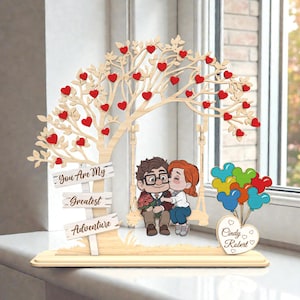 May include: A wooden decorative piece featuring a tree with red heart-shaped leaves and a swing with a couple. The sign reads "You Are My Greatest Adventure." A heart-shaped balloon bouquet and a heart with the names "Cindy Robert" are also included.