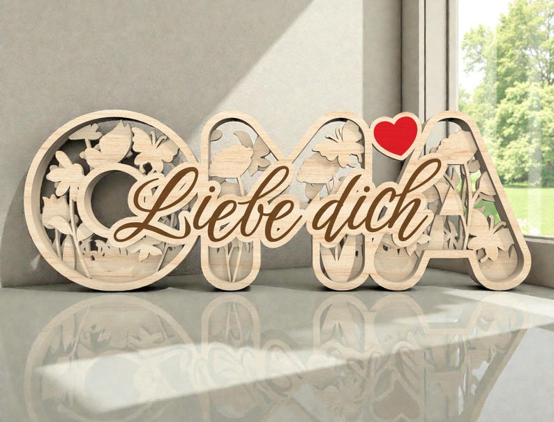 Op de afbeelding: Houten bord met de tekst "OMA Liebe dich" en een rood hart. De letters zijn lichtbruin met uitgesneden bloemen- en vlindermotieven. De woorden "Liebe dich" zijn in een sierlijk lettertype geschreven, wat een decoratief tintje geeft.