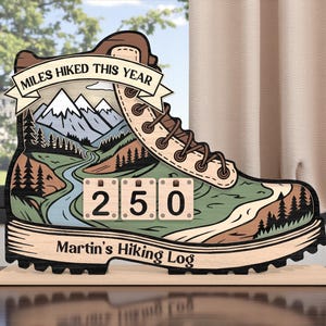 Puede incluir: Un letrero de madera con forma de bota de senderismo con el texto "MILES HIKED THIS YEAR" en una pancarta. La bota presenta una escena de montaña y río, con el número "250" mostrado. El letrero también incluye el texto "Martin's Hiking Log".