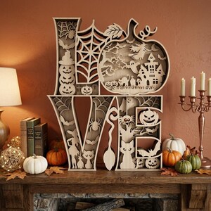 May include: A laser-cut wooden sign spelling the word LOVE, featuring intricate Halloween-themed cutouts including pumpkins, spider webs, bats, a haunted house, a witch, a cat, and a ghost within each letter, finished in a natural light wood tone.
