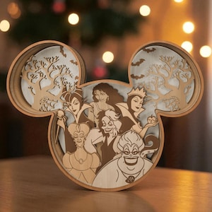 Könnte beinhalten: Mehrschichtiges Holzkunstwerk in Form von Mickey Mouse-Ohren mit Disney-Bösewichten. Das Design umfasst Bäume, Fledermäuse und Porträts der Charaktere in Braun- und Beigetönen. Das Stück wird auf einer Holzoberfläche präsentiert.
