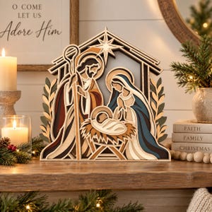 May include: A multi-layered wooden nativity scene featuring stylized figures of Joseph, Mary, and the infant Jesus in a manger under a star. The design uses natural wood tones, deep blue, and dark red accents to create a dimensional display.
