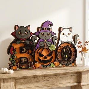 May include: A multi-layered wooden Halloween decoration featuring three cats: one in a vampire cape, one in a purple witch hat, and one in a ghost costume. The cats are positioned above the letters B, O, and O, with a carved pumpkin and haunted house.
