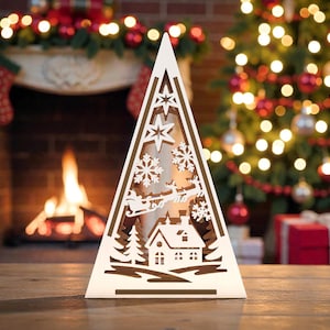 May include: A white, triangular Christmas tree decoration with cut-out designs of snowflakes, stars, a house, and Santa's sleigh. The decoration is illuminated, with a fireplace and Christmas tree in the background.