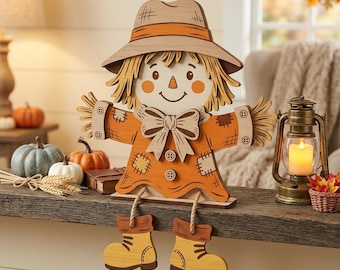 May include: A wooden scarecrow shelf sitter decoration featuring a tan hat, a bright orange shirt with a large bow, and two buttons. The figure has straw-like hair, stitched patches on the sleeves, and dangling legs with yellow boots attached by rope.