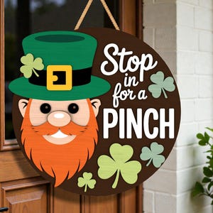 May include: A circular wooden door sign for St. Patrick's Day, depicting a leprechaun with a green hat, orange beard, and the words "Stop in for a Pinch". The sign is decorated with shamrocks and has a hanging rope.
