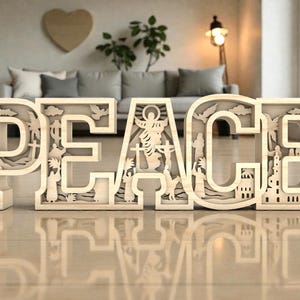 Puede incluir: Escultura de madera clara con la palabra «PAZ» en mayúsculas. Las letras están talladas con imágenes religiosas, incluyendo figuras, cruces y edificios. La escultura se encuentra sobre una superficie reflectante, reflejando la palabra.