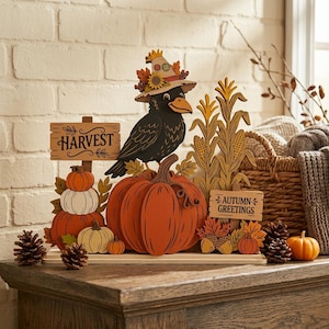 May include: A wooden tabletop decoration featuring a black crow wearing a hat, perched on a large orange pumpkin. The display includes corn stalks, smaller pumpkins, pinecones, and two signs with the text HARVEST and AUTUMN GREETINGS.