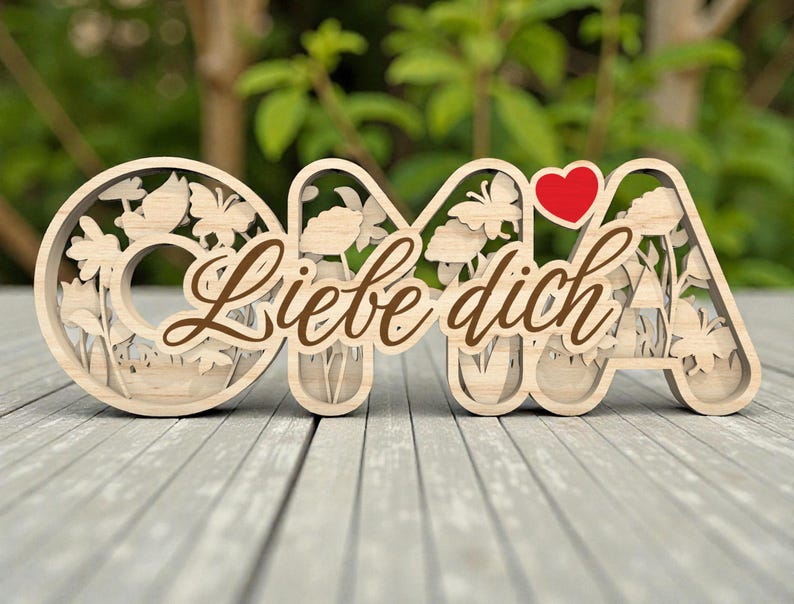 Op de afbeelding: Houten decoratief bord met de tekst "OMA" met bloemen- en vlinderuitsparingen en een rood hart. De woorden "Liebe dich" zijn in bruin script over het bord geschreven. Het bord staat op een grijs houten oppervlak.