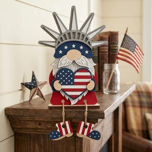 May include: A wooden gnome figurine in red, white, and blue, holding a heart-shaped American flag. The gnome has a white beard, a blue hat with stars, and star-spangled boots. A patriotic decoration for the home.