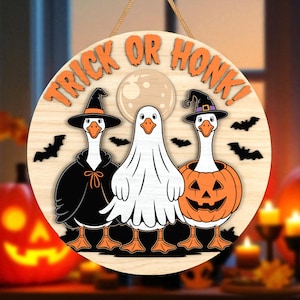 May include: Round wooden Halloween sign with the text "Trick or Honk!" featuring three geese in costumes: a witch, a ghost, and a jack-o'-lantern. The sign includes bats and a full moon. A jute rope is attached for hanging.