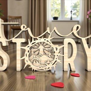 Puede incluir: Obra de arte de madera que deletrea "true story" con una representación detallada de una corona de espinas y una escena religiosa. Las letras son de color claro y la escena está intrincadamente cortada. Piezas rojas y rosas en forma de corazón están esparcidas en el suelo de madera.