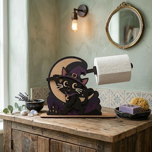 May include: A wooden toilet roll holder featuring a black cat in a witch's hat and cape, set against a crescent moon. The holder is on a wooden base. The cat is holding a broom. The holder is attached to a roll of toilet paper.