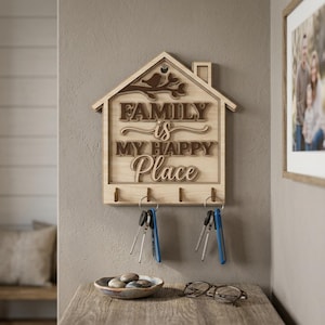 May include: Wooden key holder in the shape of a house with the words "FAMILY is MY HAPPY Place" in a layered design. The key holder has four hooks and is mounted on a gray wall. Keys with blue fobs hang from the hooks.