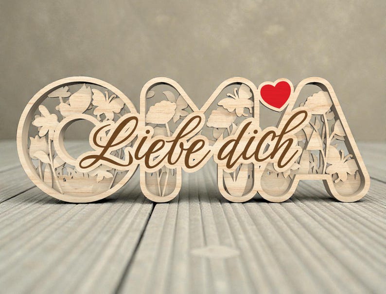 Op de afbeelding: Houten decoratief bord met het woord "OMA" en de zin "Liebe dich" in bruin script. De letters zijn uitgesneden met bloemen- en vlindermotieven. Een rood hart is boven de letter "A" geplaatst.