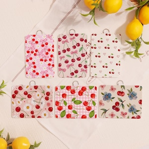 May include: Six rectangular tags with silver loops, each with a cherry design. Patterns include pink bows, hearts, daisies, and gingham. The tags are arranged on a white surface with lemons in the background.