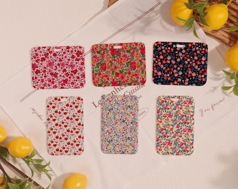 May include: Six rectangular floral patterned phone cases in various colors, including pink, red, navy, and yellow. Each case features a different floral design. The cases are arranged on a white cloth with text and lemons.