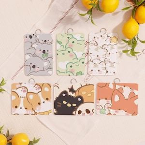 Puede incluir: Seis tarjeteros rectangulares con varios diseños de animales de dibujos animados, incluyendo koalas, ranas, tigres, corgis, gatos y zorros. Cada tarjetero tiene un anillo plateado en la parte superior. Los tarjeteros están sobre una superficie blanca con limones en el fondo.