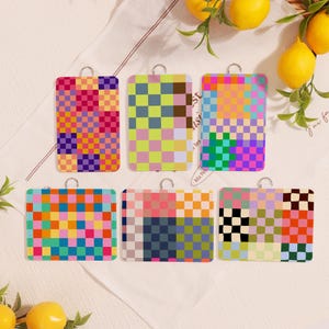 Może przedstawiać: Sześć prostokątnych, kolorowych etui na karty z tkanymi wzorami i srebrnymi metalowymi pętelkami. Wzory obejmują wzory szachownicy w różnych kolorach, takich jak różowy, niebieski, zielony, pomarańczowy i fioletowy. Cytryny i zieleń w tle.