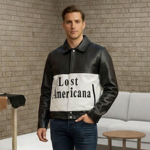May include: A black and white leather jacket with the text "Lost Americana" on the front. The jacket has a classic collar and a button closure. The person is wearing dark blue jeans and black shoes.