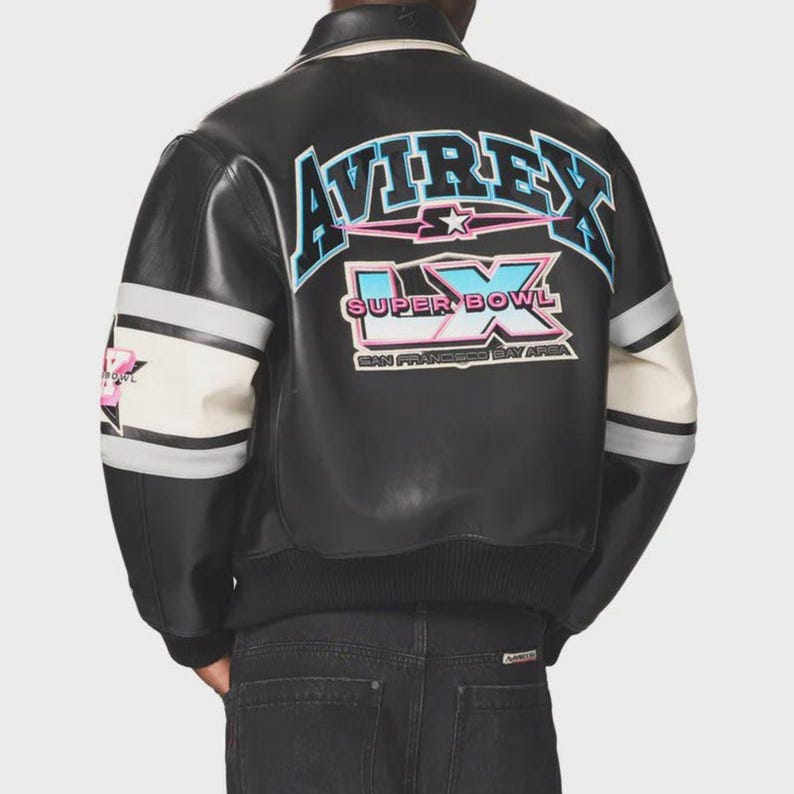 Pu&ograve; includere: Giacca in pelle nera con maniche a righe bianche e grigie. La parte posteriore presenta la scritta "AVIREX" sopra "SUPER BOWL LX SAN FRANCISCO BAY AREA" in lettere blu, rosa e bianche. La giacca ha colletto e polsini a coste.