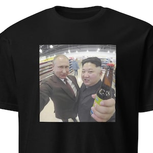 Puede incluir: Una camiseta negra con una foto de dos hombres en una tienda de comestibles. El hombre de la derecha sostiene una botella de cerveza.