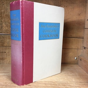 May include: A vintage hardcover cookbook titled "Amy Vanderbilt's Complete Cookbook" with a white cover and a blue and gold spine.