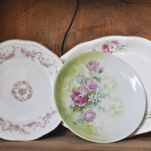 May include: Three vintage porcelain plates with floral designs. The plates are white with pink and green floral patterns. The plates are arranged in a stack, with the largest plate on the bottom and the smallest plate on top.