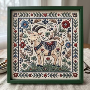 Könnte beinhalten: Ein quadratisch gerahmtes Stickbild mit einer zentralen Ziegenfigur in Creme-, Braun- und Blautönen. Die Ziege ist von einer symmetrischen Blumen- und Blattbordüre in Rot, Blau und Grün auf cremefarbenem Stoff umgeben, eingefasst in einen dunkelgrünen Rahmen.
