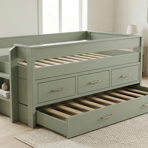 Puede incluir: Una estructura de cama verde salvia con tres cajones y una cama nido extraíble. La cama tiene una escalera incorporada con estantes. Los cajones y la cama nido tienen tiradores dorados. La estructura de la cama es de madera.