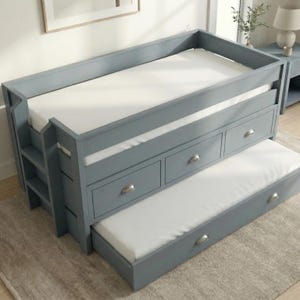 Può includere: Un letto a soppalco grigio con scala integrata e tre cassetti. Il letto ha un letto estraibile sottostante. I materassi sono bianchi. La struttura del letto è verniciata di grigio chiaro.