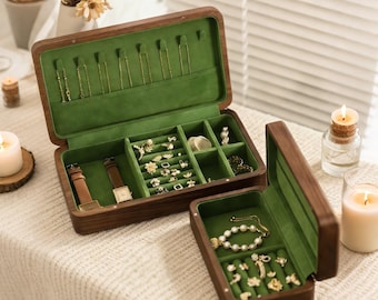 May include: Wooden jewelry boxes with green velvet lining. The open box displays necklaces, rings, earrings, and watches. The boxes are brown with a rectangular shape. The jewelry is gold and silver. The boxes are on a cream-colored surface.